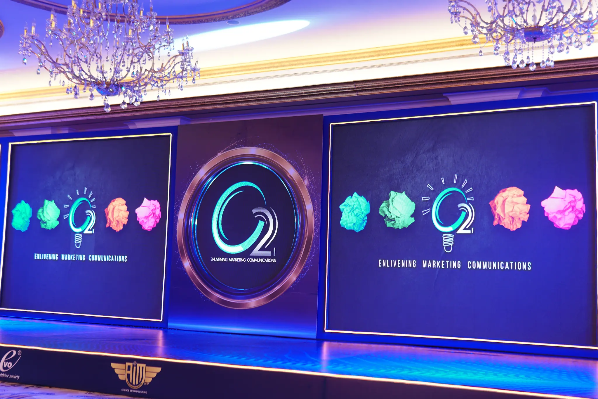 Close view of the Fast Forward stage: linked LED panels in deep blue with an illuminated centre ring, framed by gold-edged set panels and crystal chandeliers overhead.