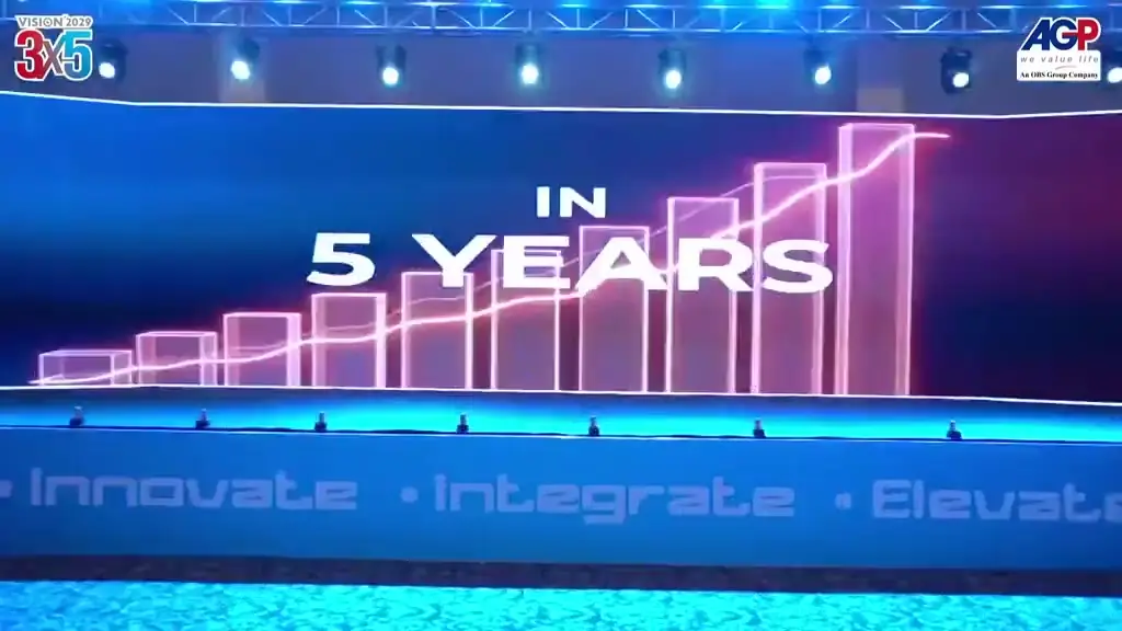 Footage from the Vision 2029 annual meeting: a wide LED stage carrying motion graphics above a full auditorium of seated delegates, with stage lighting and effects.