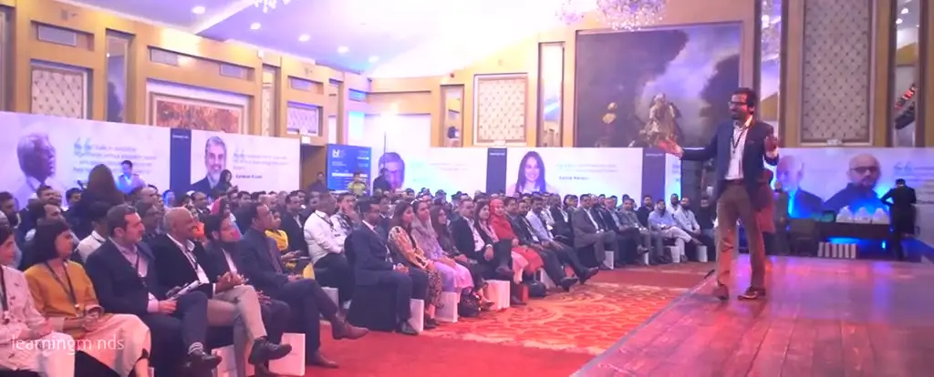 Footage from the Insights Business Forum 2019: a speaker addressing a full auditorium from a branded stage, with delegates seated in rows and the forum identity carried on the backdrop.