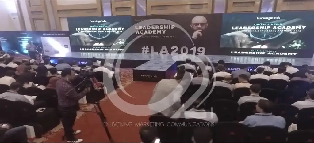 Footage from Leadership Academy 2019: a hotel ballroom seated to capacity in theatre rows, facing a triple-panel LED wall carrying the programme identity.